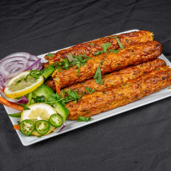 Indian seekh kebabs garnished with cilantro, lemon, red onion, and green peppers on a white plate.