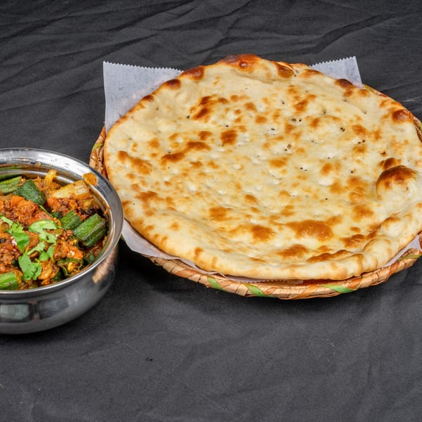 Indian okra curry in a metal bowl next to a large piece of naan bread in a woven basket.