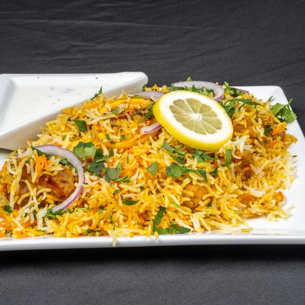 Indian chicken biryani with lemon, red onion, and cilantro, served with raita.