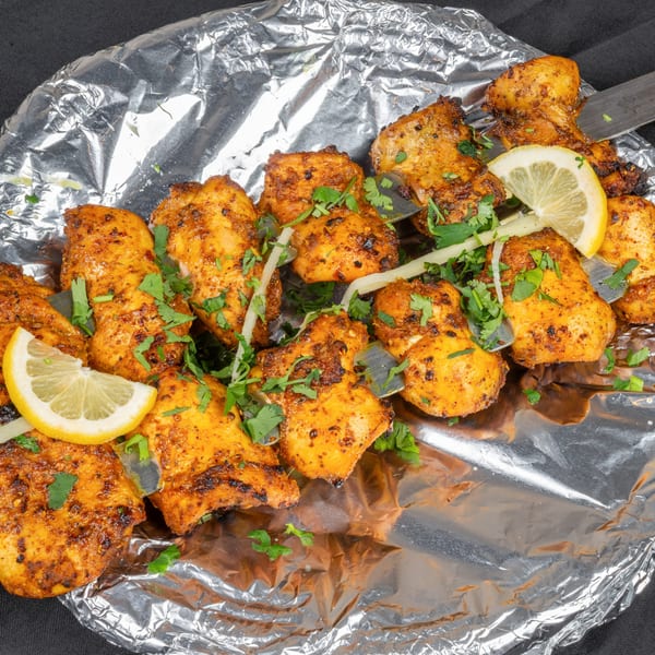 Indian chicken tikka skewers with cilantro, lemon, and onions on aluminum foil.