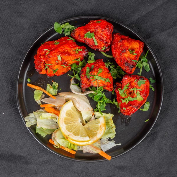 Indian chicken tikka pieces with cilantro, lemon, and salad on a black plate.