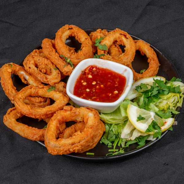 Crispy fried calamari rings with a side of sweet chili sauce, fresh lettuce, and lemon wedges.