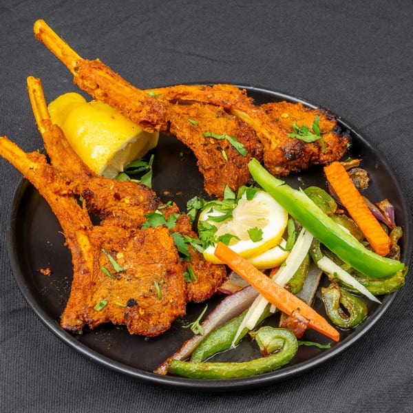 Indian lamb chops with lemon wedges, green peppers, and carrots on a black plate.